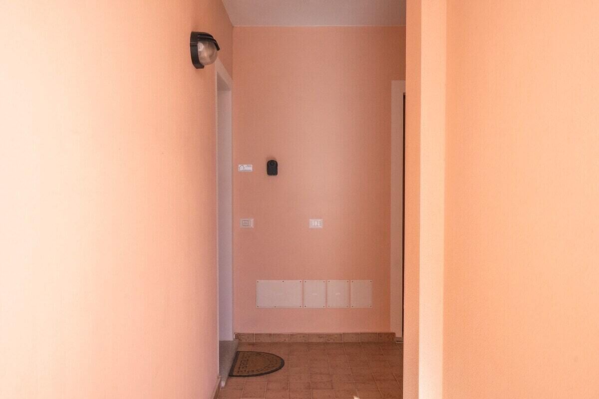 Un passadís estret amb una porta al final, un lluminari fixat a la paret i un detector de fum a la paret.