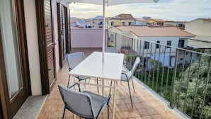 Un balcón con mesa y sillas, una sombrilla grande y vistas de edificios circundantes.