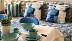 Un comedor con una mesa preparada para cuatro personas, una planta en maceta y un sofá con cojines estampados.