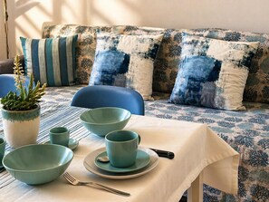 A dining area with a table set for four, a potted plant, and a sofa with patterned cushions.
