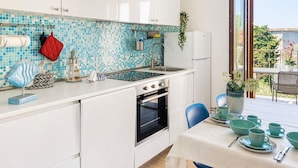 Una cocina moderna con armarios blancos, un backsplash de mosaico azul y un comedor con mesa lista para cuatro.
