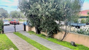 A gated driveway with a paved path, a tree-lined area, and parked vehicles.