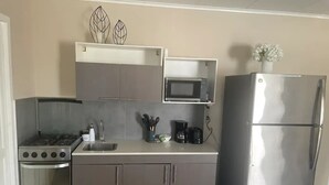 A compact kitchen with a gas stove, microwave, and stainless steel refrigerator. - Taminaka Comfortable III (Oranjestad)