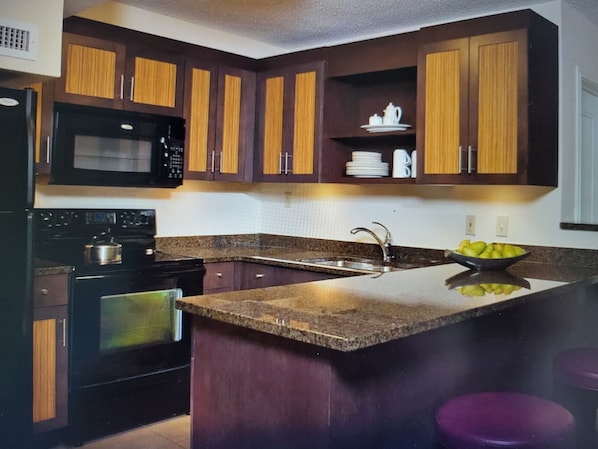 A kitchen with dark wooden cabinets, a black microwave, a stove, and a granite countertop.