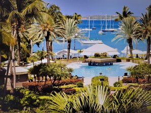 A resort with a swimming pool, palm trees, and boats in the background.