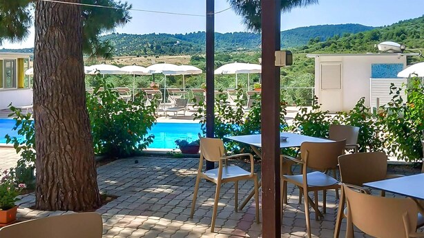 Ein Außenbereich mit Terrasse, Pool, weißen Sonnenschirmen und beigen Stühlen.