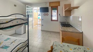 Ein kleines Zimmer mit Stockbetten, einer Kochnische und einem Fernseher.