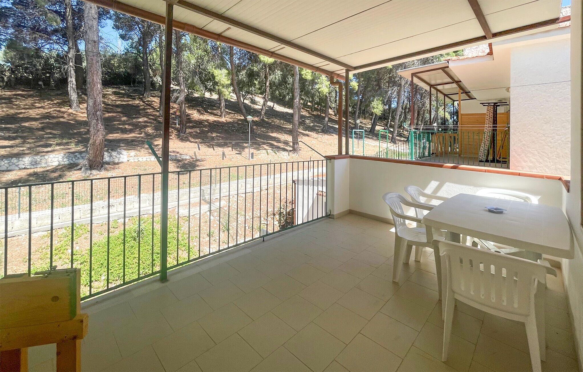A balcony with a view of a forested area, a table with chairs, and a small wooden structure.