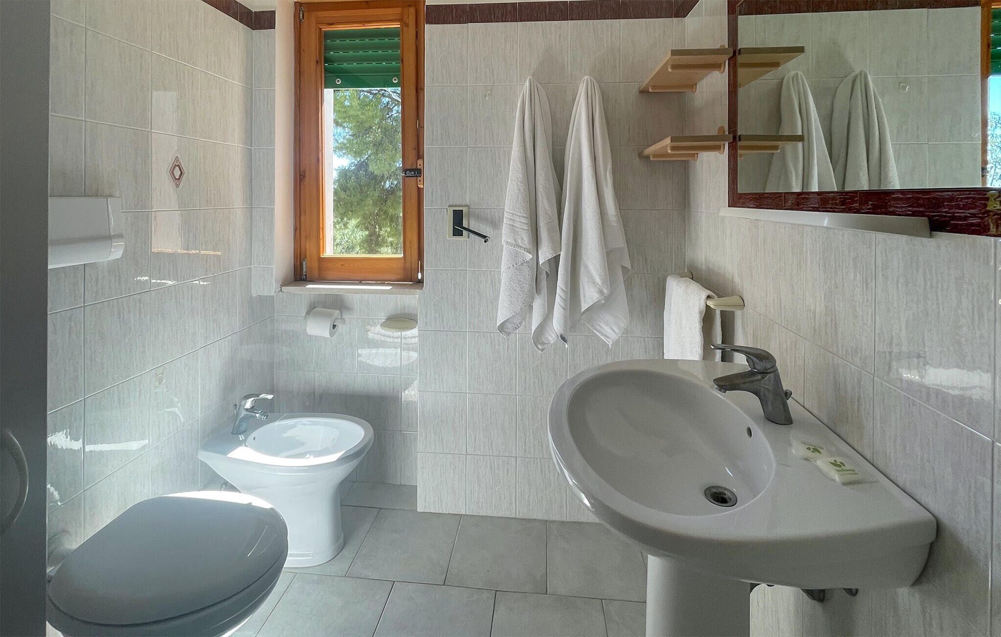 A modern bathroom with a toilet, bidet, sink, and a mirror.