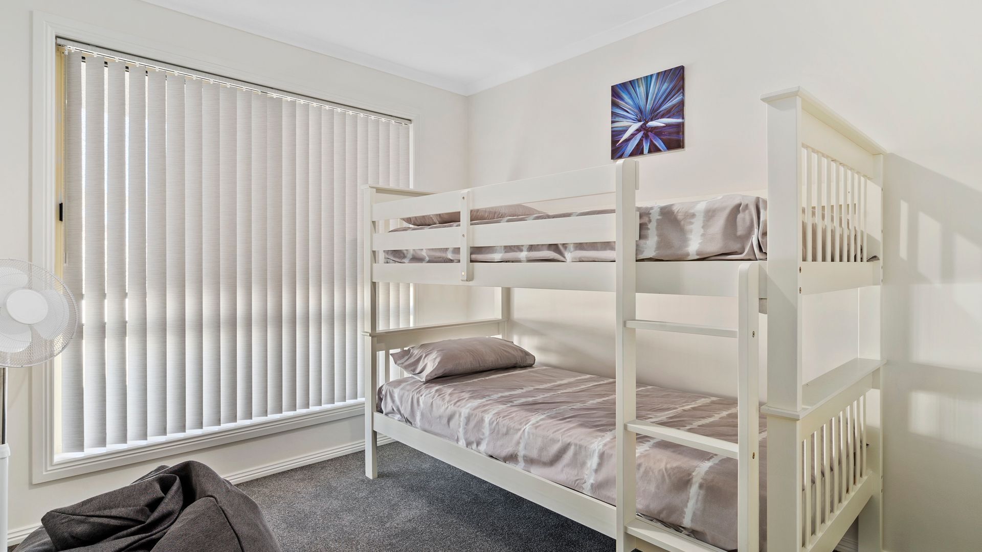 A bunk bed room with a window, a fan, and a painting on the wall.