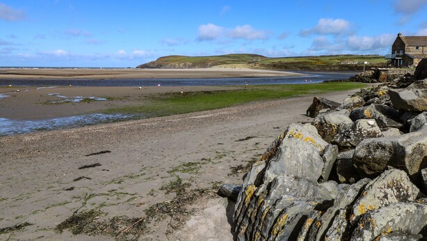 A coastal landscape with a sandy beach, rocky outcrops, and a building with a stone facade. - Parrog Bach (Newport)