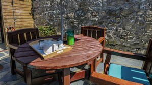 A round wooden table with chairs, a table umbrella, and a stone wall in the background. - Parrog Bach (Newport)