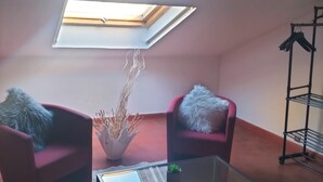Een compacte, moderne kamer met dakraam, twee rode fauteuils, een glazen salontafel en een plant.