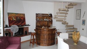 Een woonkamer met een houten bar, een open haard, een trap en een schilderij aan de muur.
