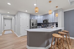 A modern kitchen with grey cabinets, stainless steel appliances, and a central island with bar stools. - 3 Bedroom 3 Bathroom Reunion 7658 (Four Corners)