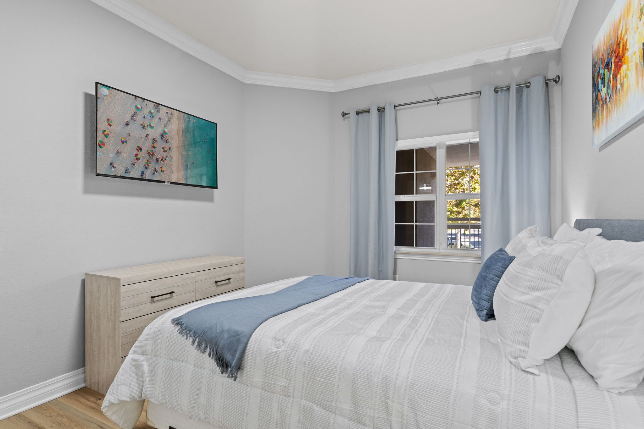 Une chambre à coucher avec un lit, une commode, une fenêtre avec des rideaux et un tableau accroché au mur.