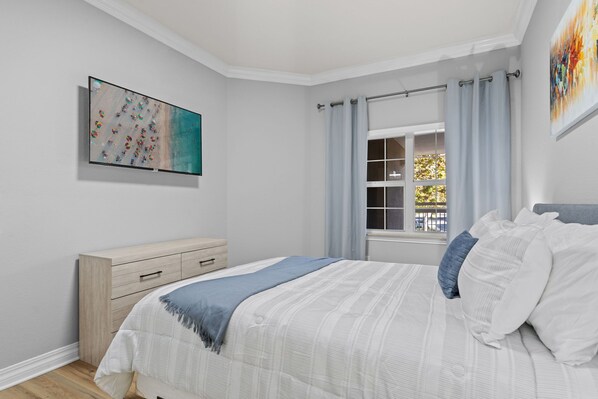 A bedroom with a bed, a dresser, a window with curtains, and a painting on the wall.