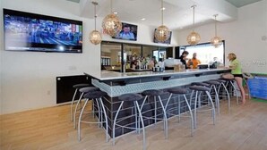 A modern bar area with a long counter, multiple stools, and pendant lighting. - 5 Bedroom 4 Bathroom Windsor at Westside 8933PW (Kissimmee)