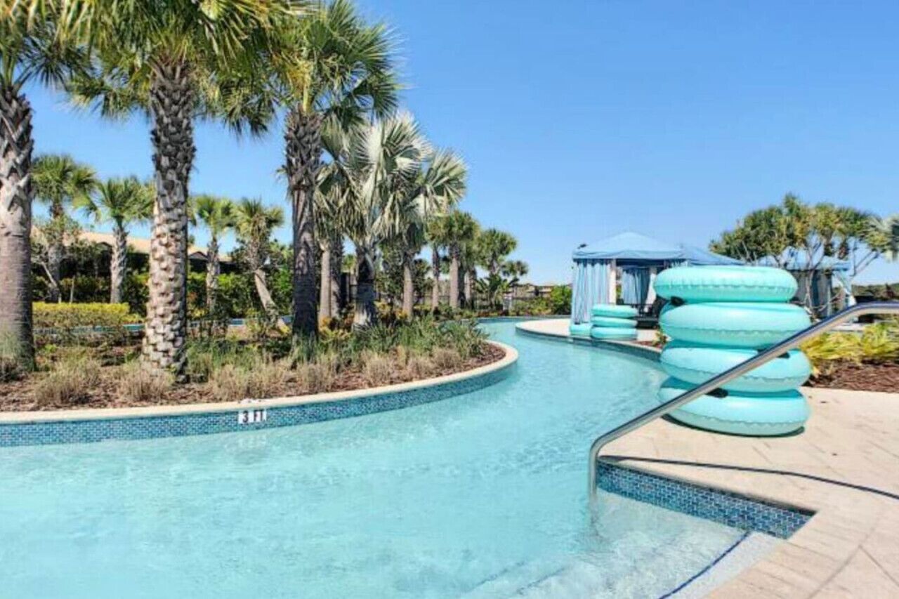 A swimming pool with a curved design, surrounded by palm trees and a gazebo.