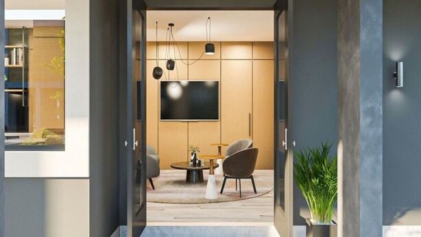 A modern interior with a flat-screen TV mounted on the wall, a round coffee table, two chairs, and a potted plant.