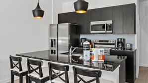 A modern kitchen with black cabinets, stainless steel appliances, a granite countertop, and black chairs.