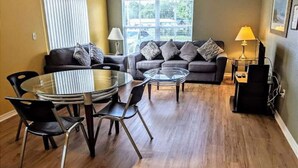 A living room with a glass-top dining table, two sofas, and a window with blinds.