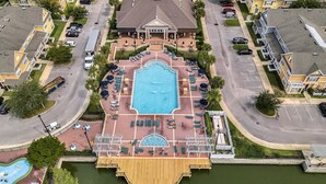 An aerial view of a hotel with a central swimming pool, multiple lounge areas, and a dock extending into a body of water.