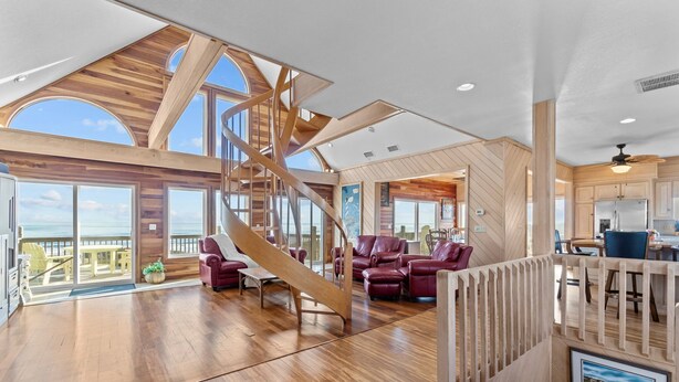 Un espacio habitable amplio con una escalera de madera, sofás de cuero y vista al océano.