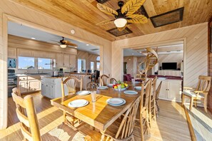 A spacious kitchen with wooden cabinets, a dining area with a large table set for six, and a spiral staircase leading to another level. - Oceanfront, Hot Tub, Beach Access, Game Room, Poker Table (Frisco)