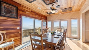 Comedor con paneles de madera, una mesa grande, sillas y vista al océano.