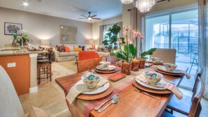 A spacious living area with a dining table set for four, a kitchen with a bar, and a large window offering a view of the outdoors. - 4 Bedroom 3 Bathroom Storey Lake 4895CT (Kissimmee)