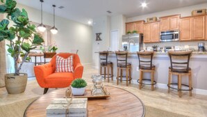 A modern kitchen with wooden cabinets, a stainless steel refrigerator, and a bar area with stools. - 4 Bedroom 3 Bathroom Storey Lake 4895CT (Kissimmee)
