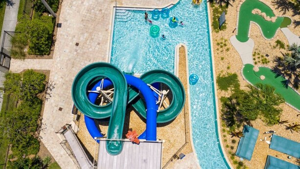 An aerial view of a water park with a large pool, a water slide, and a sandy area with lounge chairs. - 4 Bedroom 3 Bathroom Storey Lake 4895CT (Kissimmee)