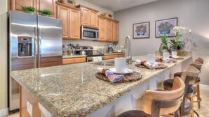 A kitchen with granite countertops, stainless steel appliances, wooden cabinets, and a bar area with chairs. - 4 Bedroom 3 Bathroom Storey Lake 4895CT (Kissimmee)