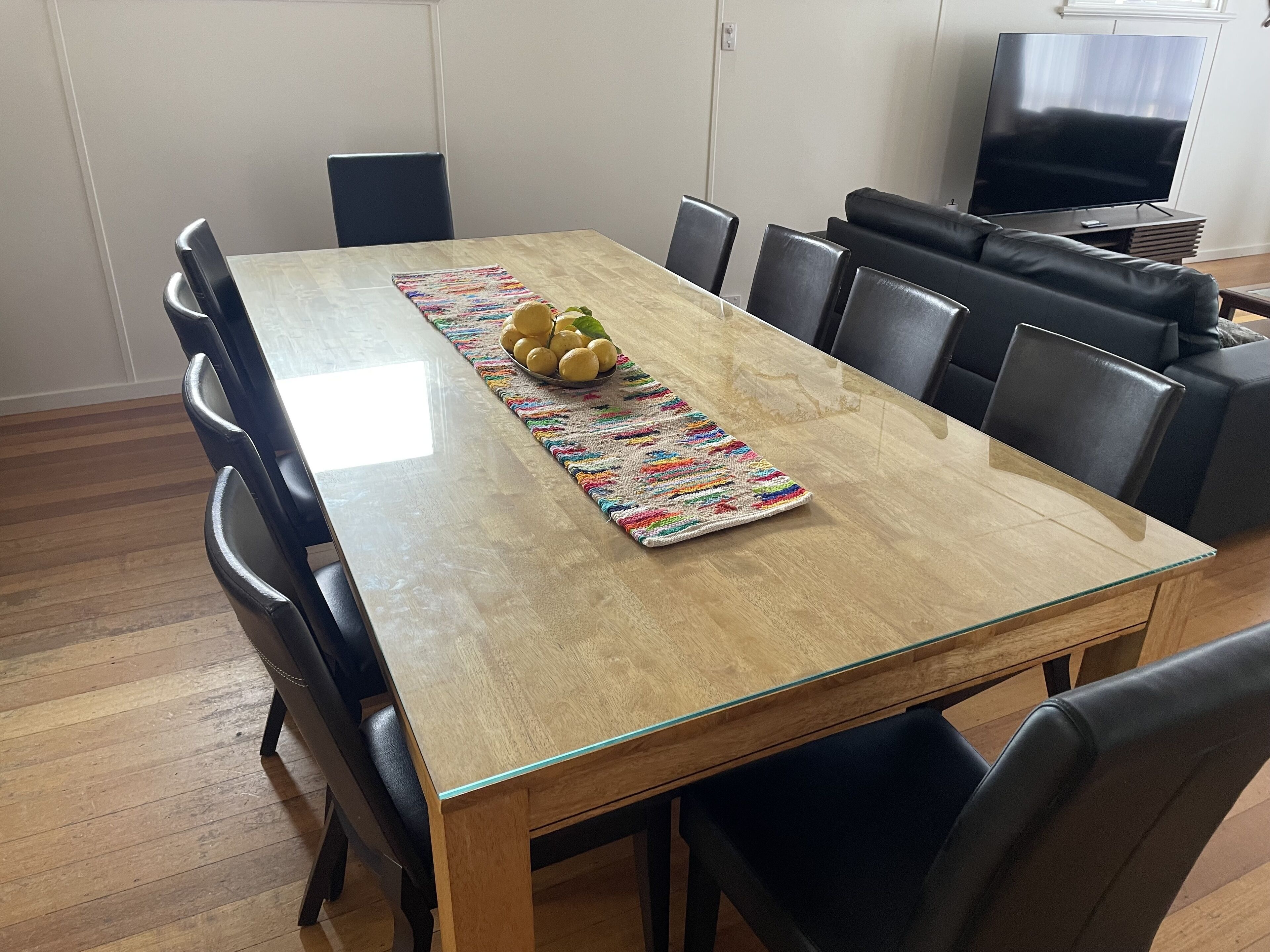 A dining area with a glass-top table, black chairs, a colorful runner, and a bowl of lemons.