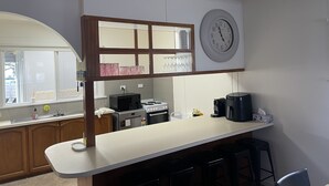 Ett kök med en vit bänkskiva, en mikrovågsugn, en kaffebryggare och en klocka på väggen.
