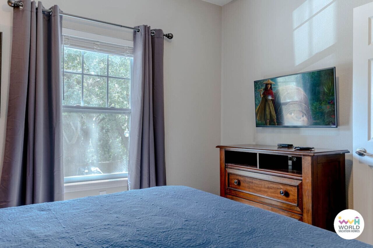 A bedroom with a bed, a wooden dresser, a window with curtains, and a painting on the wall.