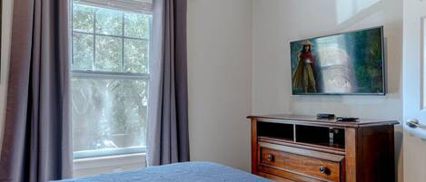 A bedroom with a bed, a wooden dresser, a window with curtains, and a painting on the wall.