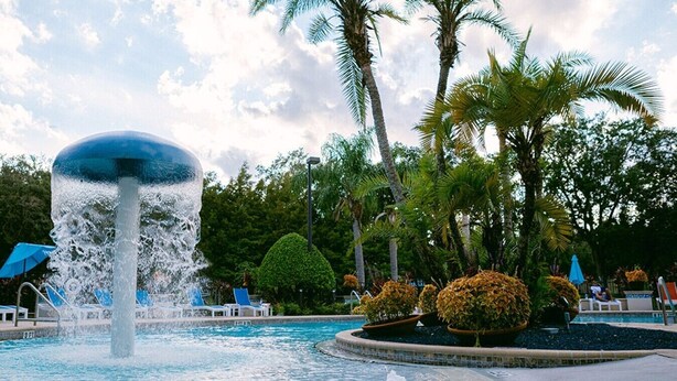 A pool with a central fountain, surrounded by palm trees and lounge chairs.