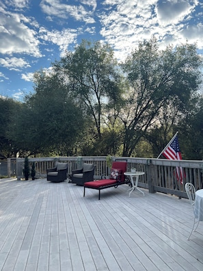 Une terrasse en bois avec des meubles d’extérieur, notamment un fauteuil rembourré rouge et un fauteuil en osier, ainsi qu’un drapeau américain.