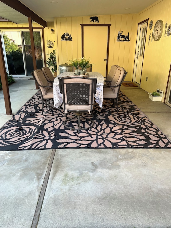 Un patio con mesa y sillas, un tapete decorativo, una planta en maceta y adornos en la pared.