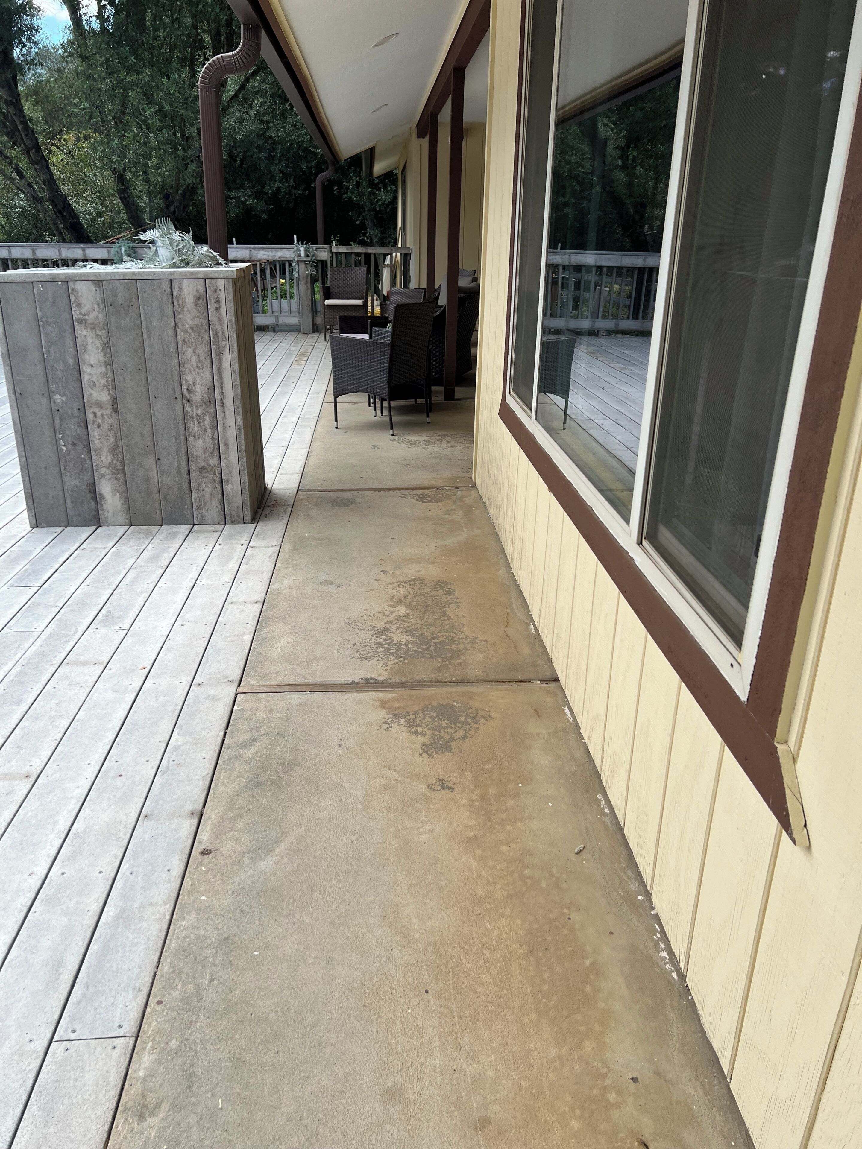 Un espace extérieur abrité, doté d’un sol en béton, d’une terrasse en bois et d’une fenêtre donnant sur la terrasse.