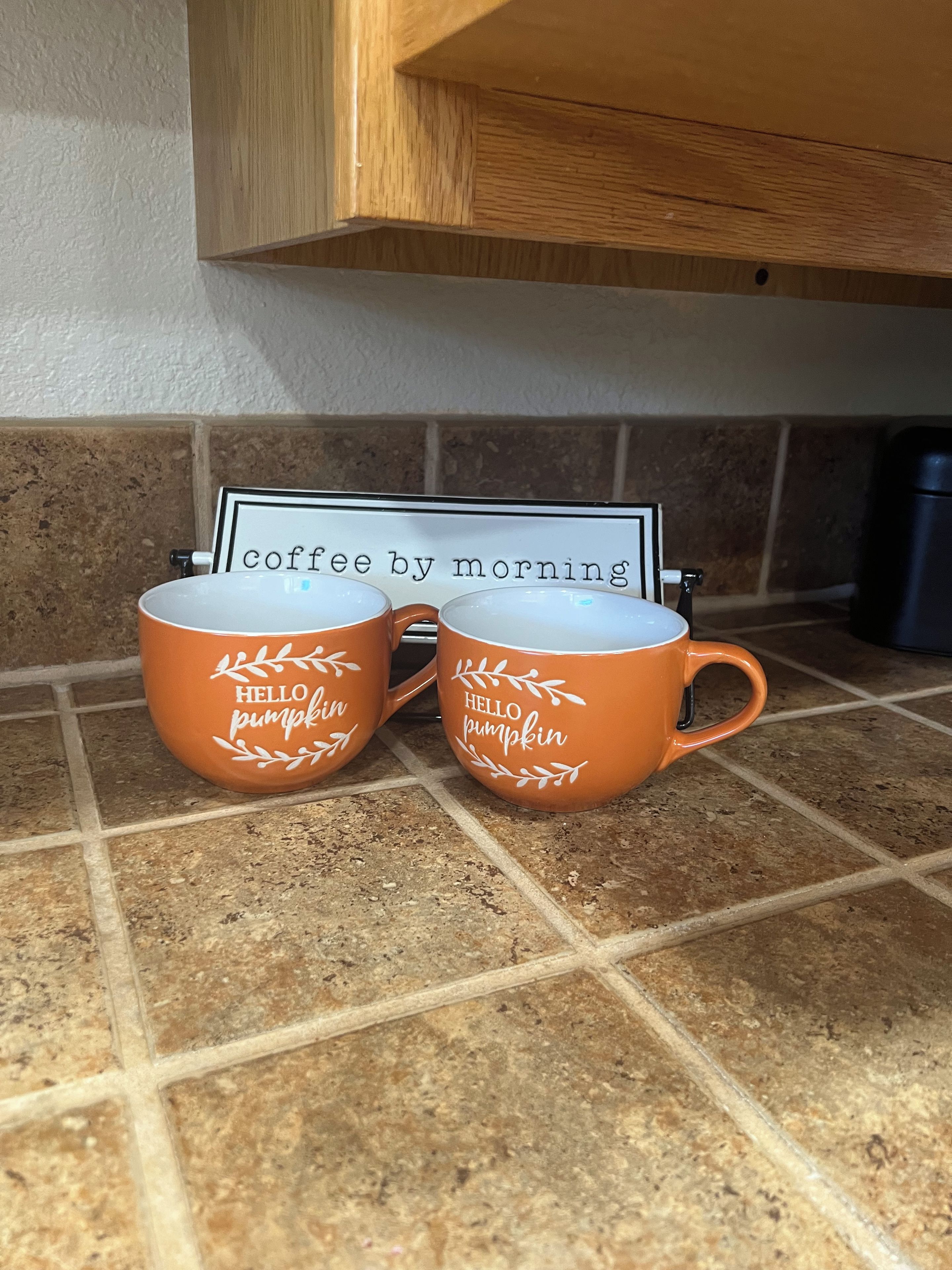Two orange coffee mugs with 'HELLO pumpkin' text on a kitchen counter.