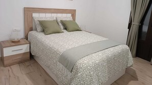 A bedroom with a bed, a nightstand, a drawer, and a window with curtains.