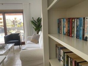 Relax in this serene living space, featuring a sofa, armchair, and bookshelf, with a balcony offering views of the surrounding area.