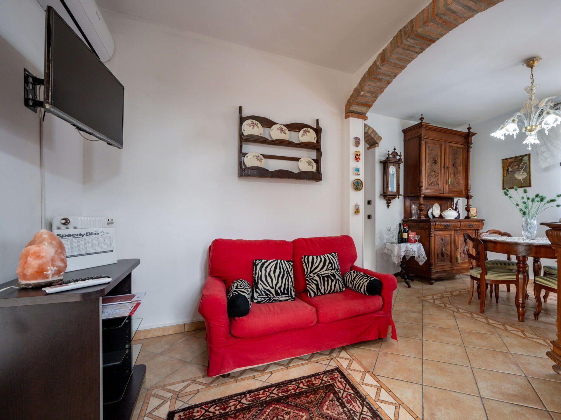 Un salon avec un canapé rouge, un téléviseur à écran plat, un meuble en bois et un coin repas comprenant une table et des chaises.