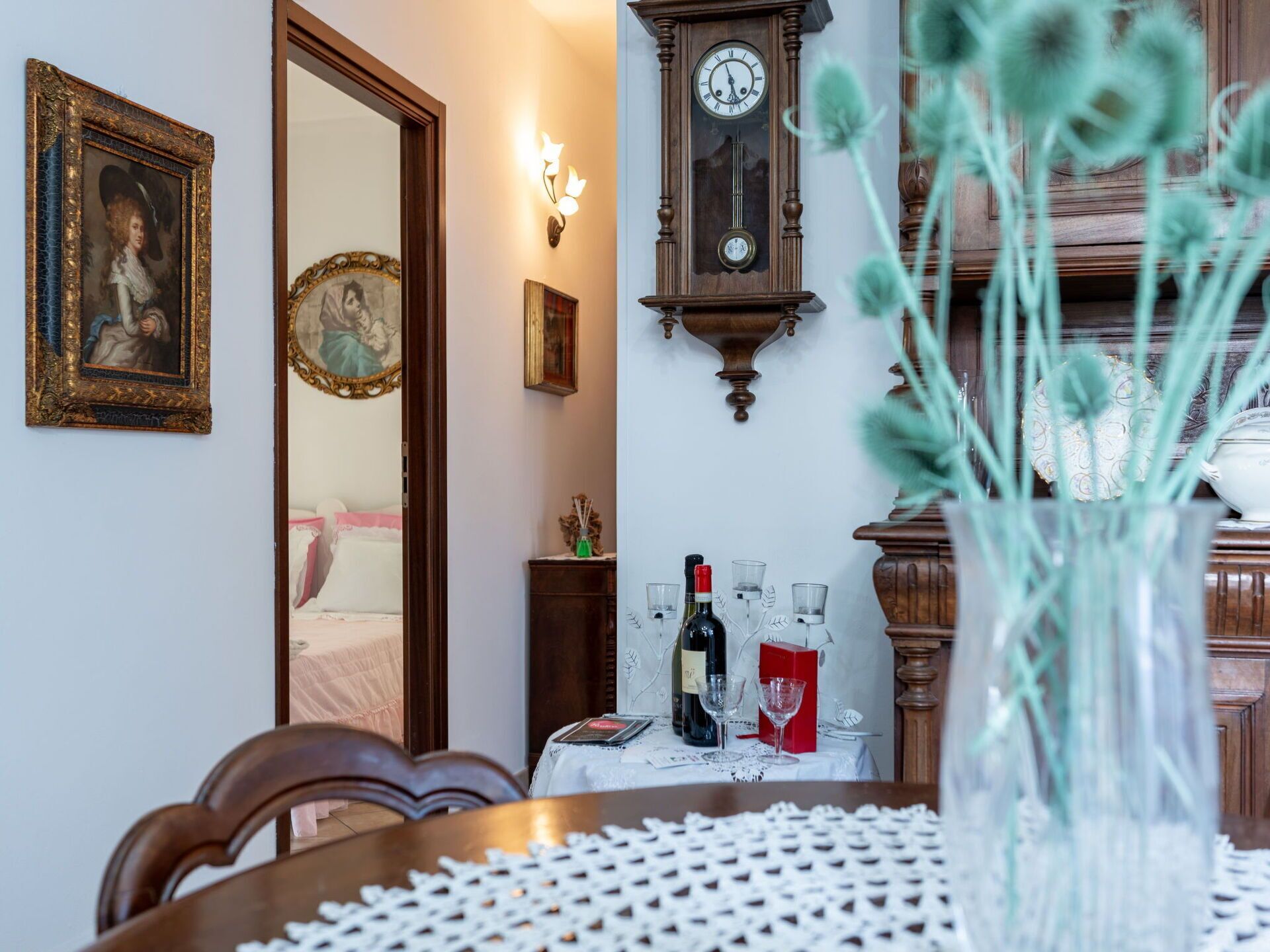 A dining area with a table set for two, a wall-mounted clock, and framed artwork.