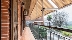 A covered balcony with a metal railing, a brick wall, and a view of a residential area. - Beautiful private villa for 4 people with A/C, private pool, WIFI, TV, patio and pets allowed (Montaldo Scarampi)