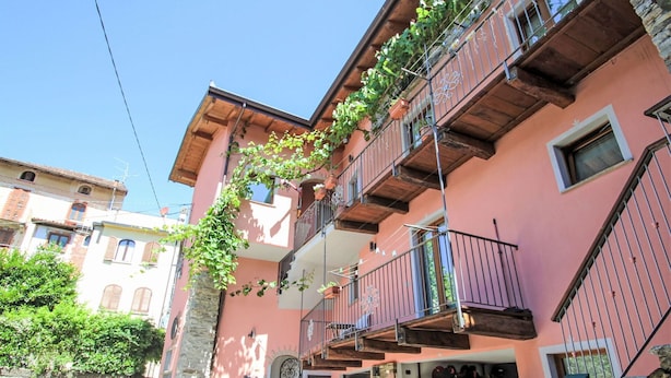 A pink building with a stone staircase, a metal gate, and a door with a decorative arch. - Nice apartment for 4 people with WIFI, TV and balcony (Dumenza)