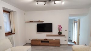 A modern living room with a flat-screen TV mounted on the wall, wooden shelves, and a decorative vase with flowers. - Nice apartment for 4 people with WIFI, TV and balcony (Dumenza)